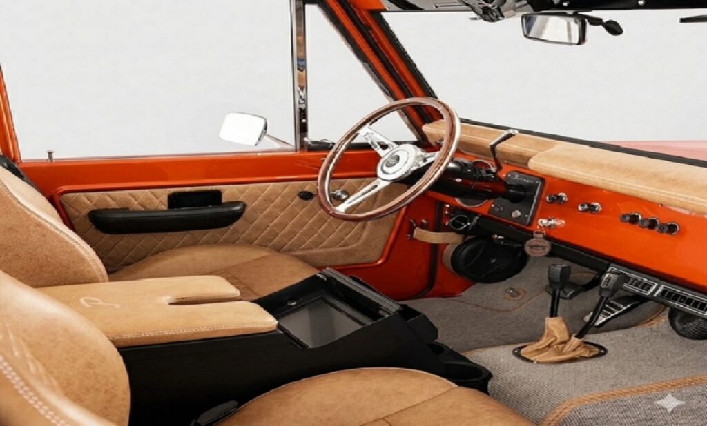 Interior view of a custom restored International Scout featuring a metallic orange dashboard, tan diamond-quilted leather door panels, saddle tan leather bucket seats, and a classic wood-rimmed steering wheel.